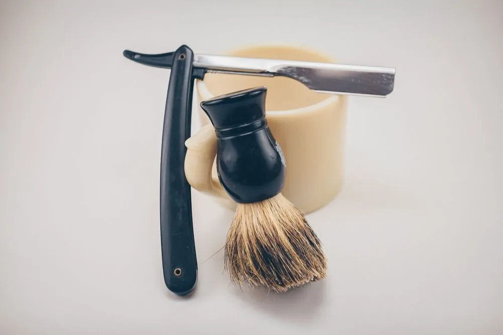 A straight razor and a shaving brush laid on a cream cloth